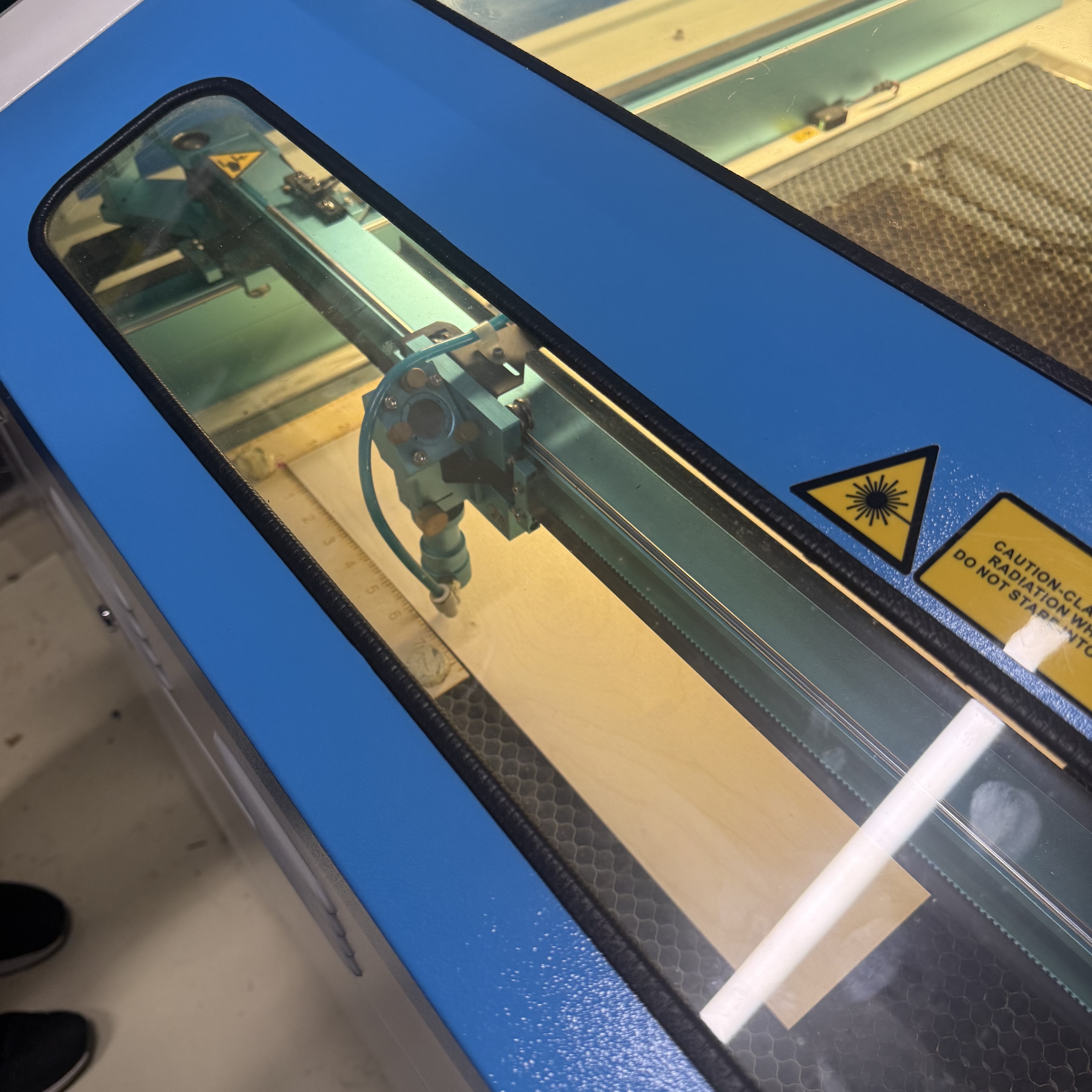 The laser cutting machine moved back and fourth rapidly to heat up, preparing itself to cut the designs into the wood.